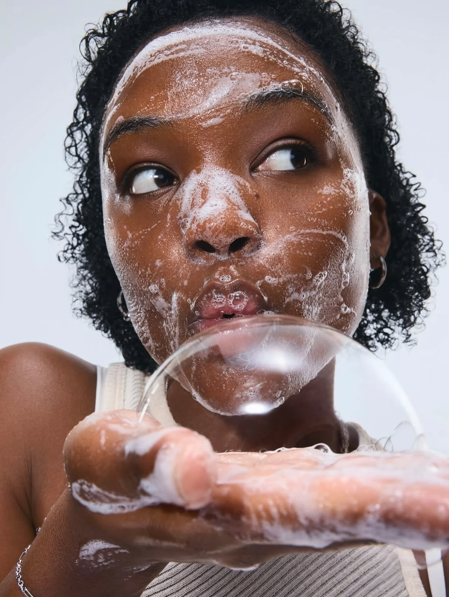 Visage couvert de mousse nettoyante, une bulle de savon au bout des lèvres